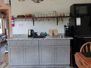 Eine Küche mit grauen Schränken, einem schwarzen Kühlschrank und einem Holzsessel.