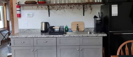 Une cuisine avec des meubles de couleur grise, un réfrigérateur noir et une chaise en bois.