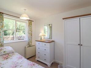 A bedroom with a bed, a dresser, a mirror, a radiator, and a wardrobe. - Walk Farm Cottage (Gloucester)
