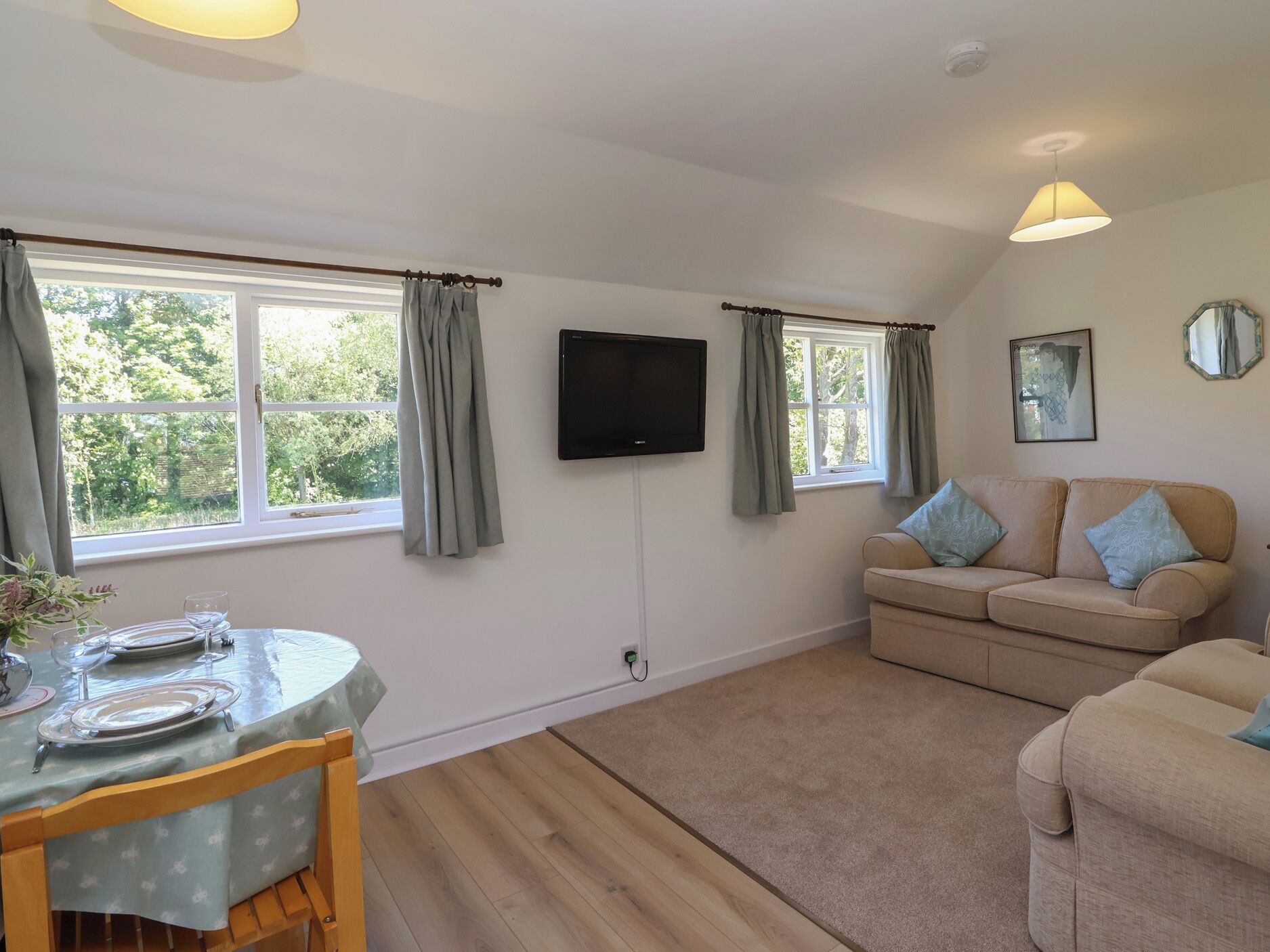 A room with a dining table set for two, a sofa, a television, and a window with curtains.