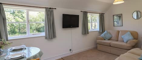 A room with a dining table set for two, a sofa, a television, and a window with curtains.