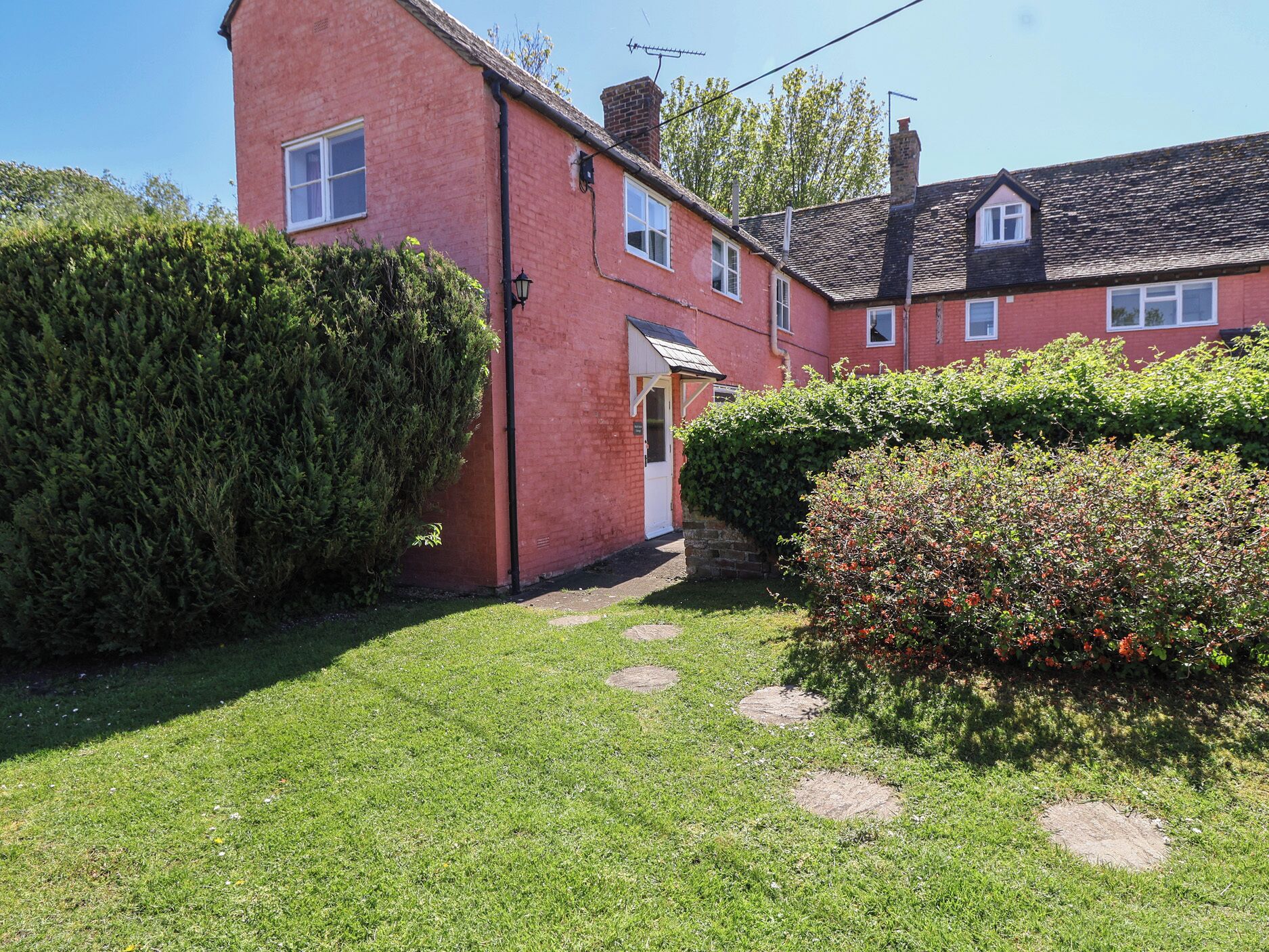 A red brick house with a small front yard, a hedge, and a bush with red berries.