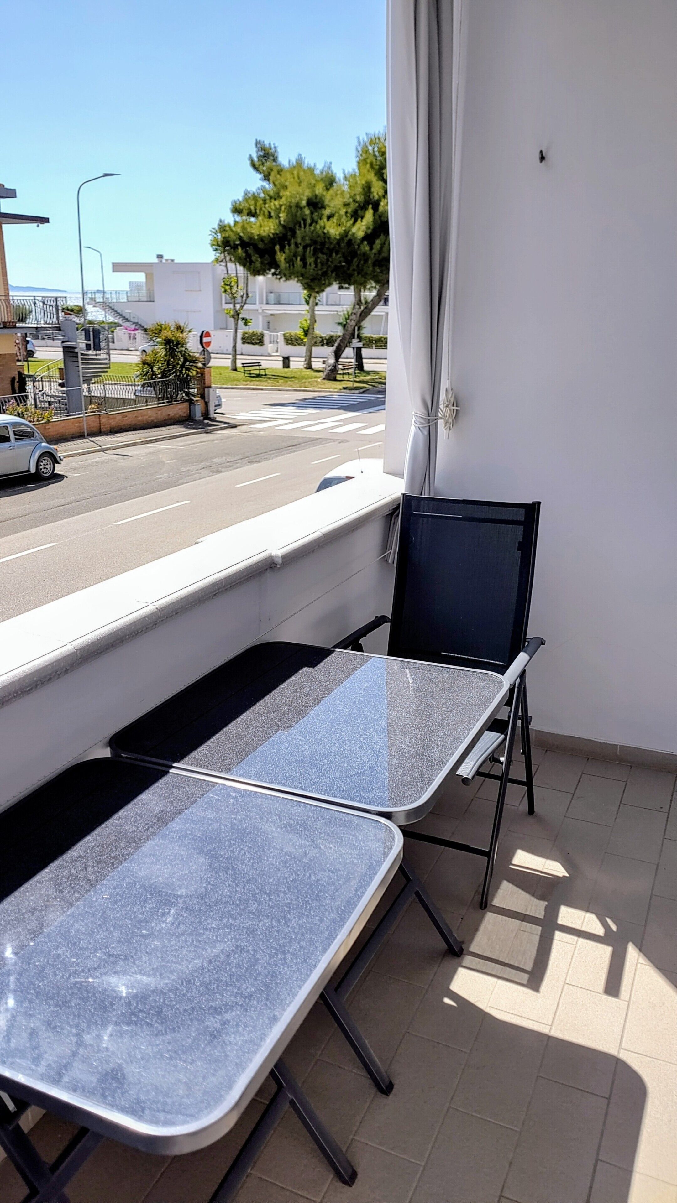 Un balcon avec deux tables et des chaises, une vue sur la rue et un immeuble en arrière-plan.
