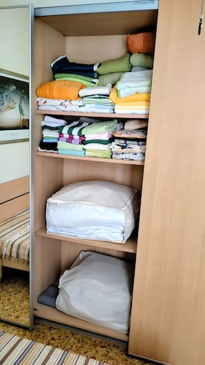 Une armoire avec plusieurs étagères où sont rangés des vêtements pliés et un matelas.