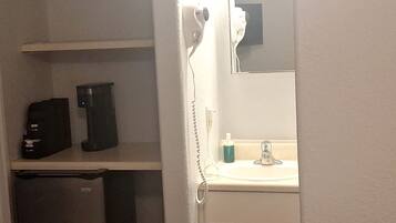 A bathroom with a sink, a mirror, a hairdryer, and a small cabinet.