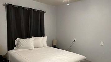 A hotel room with a bed, a ceiling fan, a nightstand, and a wall socket.