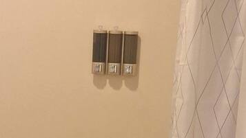 A bathroom with a shower curtain, a towel on the floor, and two wall-mounted soap dispensers.