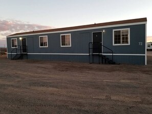 A single-story building with a flat roof, numbered 72, featuring a set of stairs leading to a door and windows along the side.