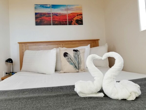 Habitación de hotel con cama, almohadas, manta, un cuadro colgado en la pared y una decoración de toallas con forma de cisne.