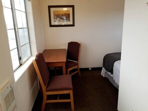 Una habitación pequeña con una mesa, dos sillas, una cama, una ventana y un cuadro en la pared.