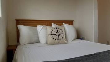 Una cama con ropa de cama blanca, un plaid gris y una almohada con motivos de brújula.