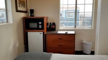 A small room with a bed, a microwave, a small refrigerator, a window with a view, and a trash bin.