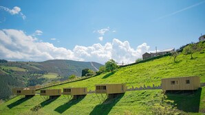 A series of wooden cabins on stilts in a grassy hilly area with a clear sky.