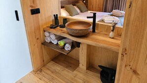 A wooden room with a large bowl sink, a bed with pillows, and neatly folded towels.
