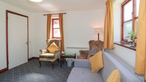 Ein Zimmer mit grauem Sofa, einem gemusterten Sessel, einem kleinen Tisch, einer Lampe und einem Fenster mit Vorhängen.