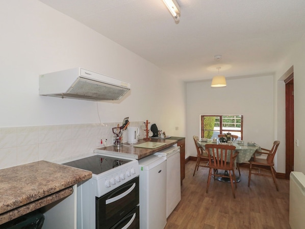 A compact kitchen with a stove, oven, and microwave, a dining table with chairs, and a window providing natural light. - Walk Close (Gloucester)