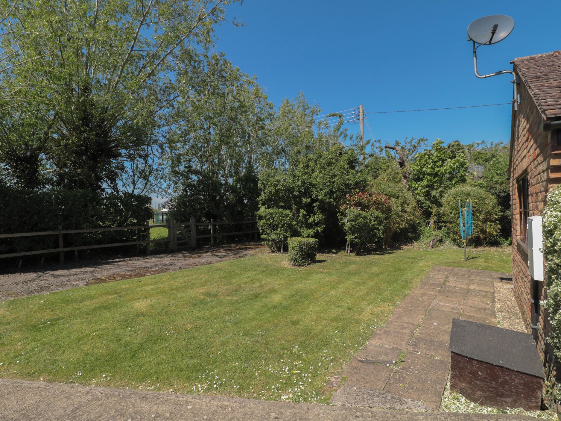 A fenced backyard with a lawn, a brick building, and a satellite dish.