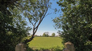Ein hölzernes Tor führt zu einem grünen Feld mit Bäumen im Hintergrund.