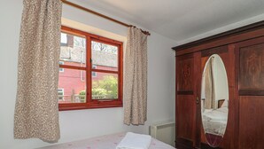 Ein Schlafzimmer mit Bett, einem Fenster mit Vorhängen, einer Heizung und einem Schrank mit Spiegel.
