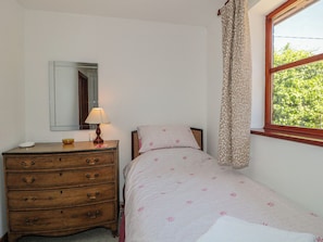 A bedroom with a wooden dresser, a bedside lamp, a bed with floral bedding, a mirror, and a window with curtains. - Walk Close (Gloucester)