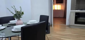 Spiseområde med et bord dækket til fire personer, en potteplante og et køkken i baggrunden.