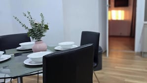 A dining area with a table set for four, a potted plant, and a kitchen in the background. - Convenient Glenroy Accommodation Ideal for Airport Travellers (Melbourne)