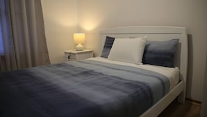 A neatly made bed with a white headboard, a bedside lamp, and a window with curtains. - Convenient Glenroy Accommodation Ideal for Airport Travellers (Melbourne)
