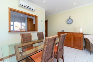 A dining area with a glass table, wicker chairs, a wooden cabinet, and a wall clock. - 1 Bed Apt With Sea Views & Communal Pool (Carvoeiro)