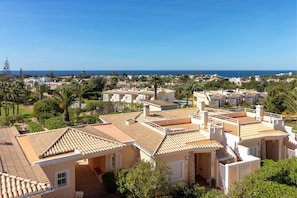 A coastal residential area with terracotta-tiled buildings, a clear blue sky, and a view of the sea.