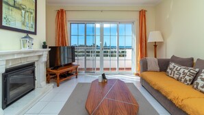 Ein Wohnzimmer mit Kamin, Fernseher, einer Couch und Blick durch große Fenster.