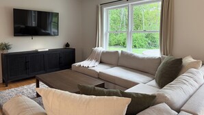 Een woonkamer met een bank, een salontafel, een televisie en een raam met gordijnen.