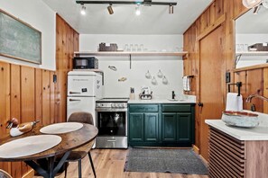 A compact kitchen with wooden cabinets, a dining table with chairs, a microwave, a stove, and a sink. - Cozy Nature-Inspired Cabins with Outdoor Spaces Near Garden of the Gods, Colorado Springs, CO (Colorado Springs)