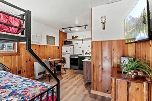 Ein kompakter Raum mit Etagenbetten, einer Küchenzeile, einem Essbereich und einem an der Wand befestigten Fernseher.