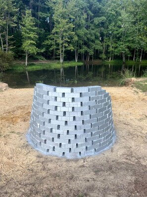 A circular brick structure in a natural setting with a body of water and trees in the background.