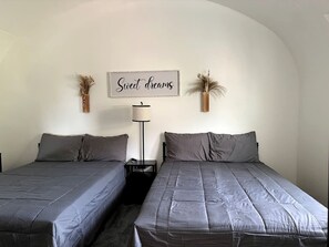 A double bed room with two beds, a bedside table, a lamp, and a wall sign.