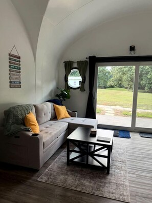 Un salon moderne avec un canapé, une table basse et une vue sur l’extérieur, accessible par une grande porte-fenêtre coulissante.