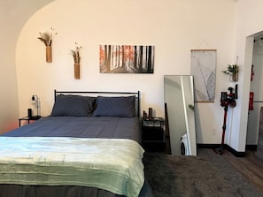 Un dormitorio con una cama, una mesita de noche, un espejo y una obra de arte colgada en la pared.