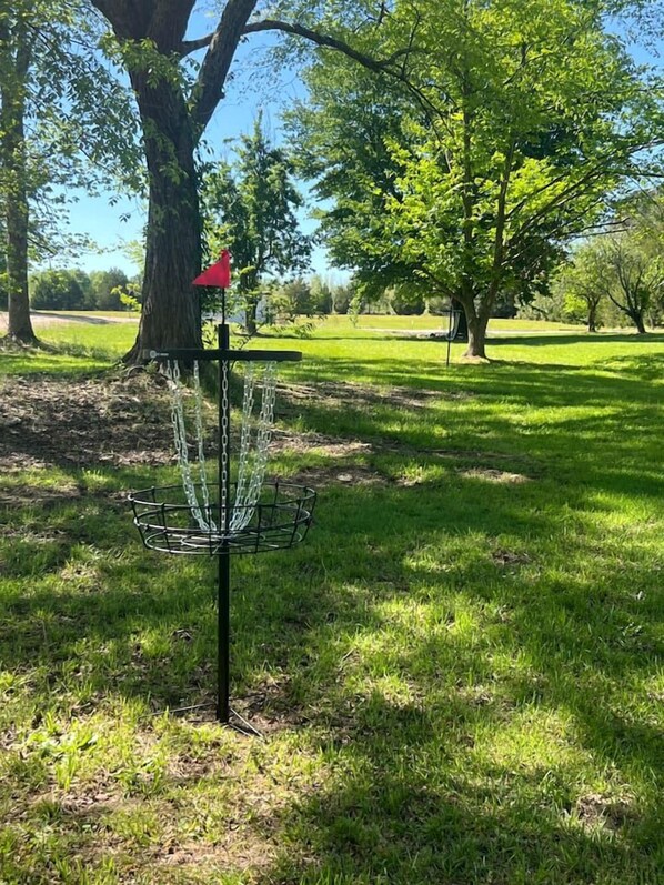 A disc golf basket in a park with trees and grass.