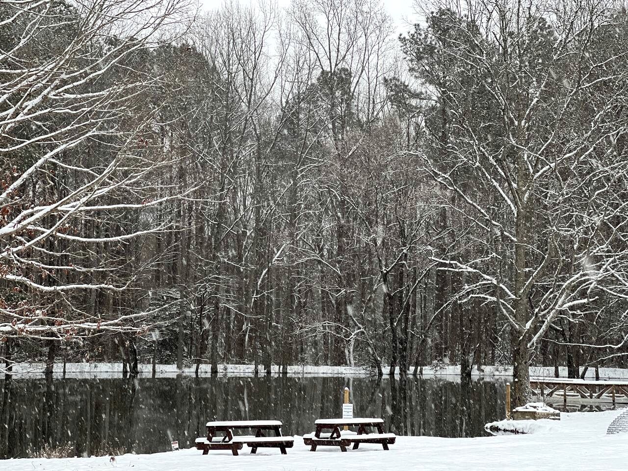 A snow-covered park with benches and a pond.