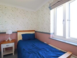 Un dormitorio con cama, mesita de noche, ventana y papel tapiz floral.