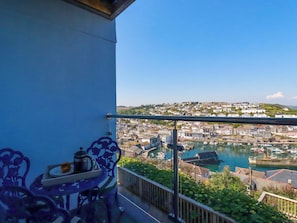 Ein Balkon mit Tisch und Stühlen, der auf einen Hafen mit Booten und Gebäuden blickt.