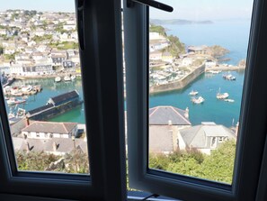 Blick aus einem Fenster auf eine Küstenstadt, inklusive Hafen mit Booten, einer Wellenbrecheranlage und Wohnhäusern.