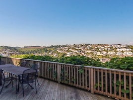 Una terraza de madera con una mesa y sillas, con vistas a un pueblo con casas y vegetación.