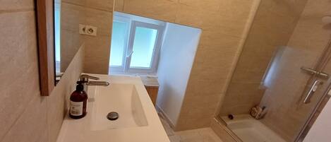 Un baño con lavamanos blanco, dispensador de gel antibacterial, ducha y ventana.