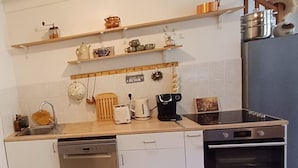 Eine kompakte Küche mit Spülmaschine, Toaster, Kaffeemaschine, Herd und Regalen mit Geschirr.