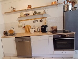Eine kompakte Küche mit Spülmaschine, Toaster, Kaffeemaschine, Herd und Regalen mit Geschirr.