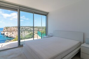 Ein Schlafzimmer mit großem Fenster, einem Bett, einem Nachttisch und einem Beistelltisch.