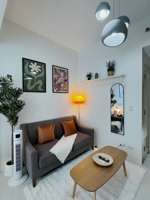 A modern living room with a grey sofa, a white air purifier, a wooden coffee table, and a mirror on the wall. - New! Serene & Cozy,  1 bedroom, Wi-Fi 350Mbps  Uptown BGC, Step from Mall BH6 (Taguig)