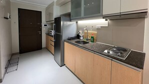 A modern kitchen with a stainless steel refrigerator, a microwave, a sink, and wooden cabinets. - New! Serene & Cozy,  1 bedroom, Wi-Fi 350Mbps  Uptown BGC, Step from Mall BH6 (Taguig)