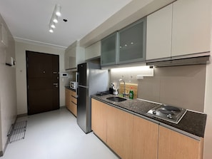 A modern kitchen with a stainless steel refrigerator, a microwave, a sink, and wooden cabinets. - New! Serene & Cozy,  1 bedroom, Wi-Fi 350Mbps  Uptown BGC, Step from Mall BH6 (Taguig)